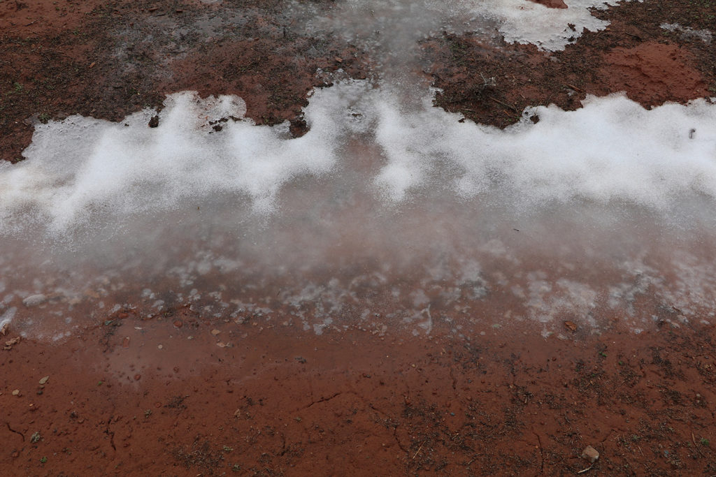 Wet red dirt with snow, ice, and water on the northside of the sheep corral.