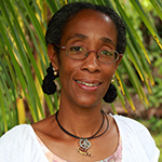 Celia is shown before green fronds of palm. Celia has medium dark skin, and black hair which is parted down the middle, and held back on either side in short a braid or bun. Celia wears a white scoop-necked blouse, and two necklaces of black cord, one bearing a silver or palegreen round pendant. 